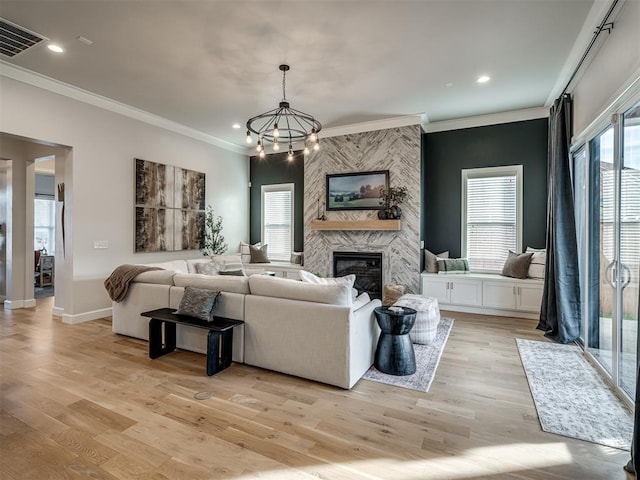 living room featuring ornamental molding, a fireplace, light hardwood / wood-style flooring, and a notable chandelier