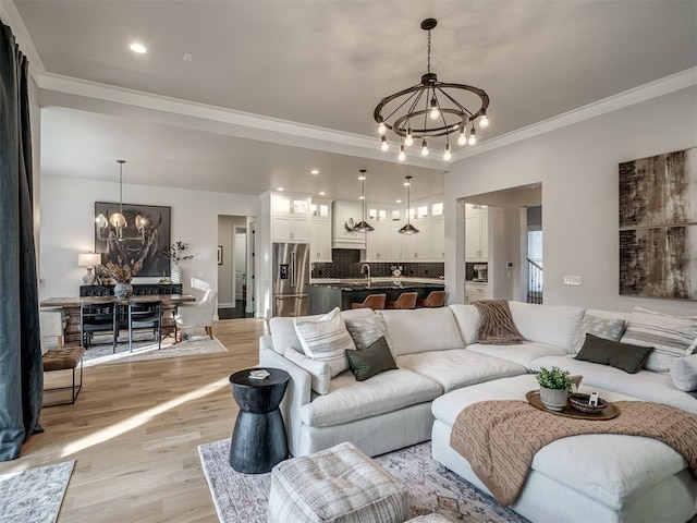 living room featuring light wood-type flooring, sink, crown molding, and a notable chandelier