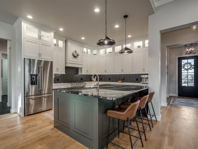 kitchen featuring white cabinets, dark stone countertops, high quality fridge, and a center island with sink