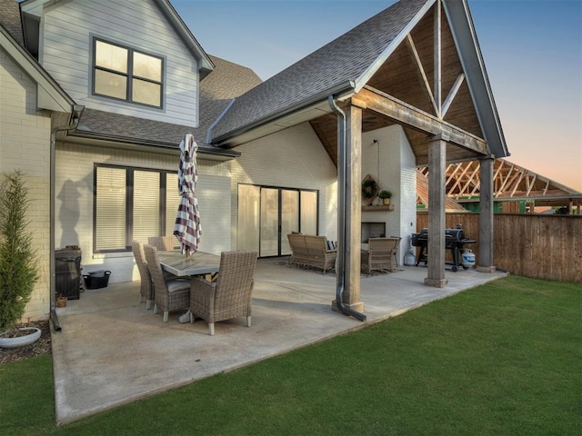 back house at dusk featuring a patio area, a large fireplace, and a lawn