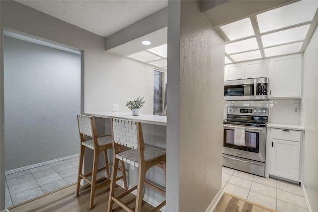 kitchen with white cabinets, a kitchen breakfast bar, decorative backsplash, light tile patterned floors, and stainless steel appliances