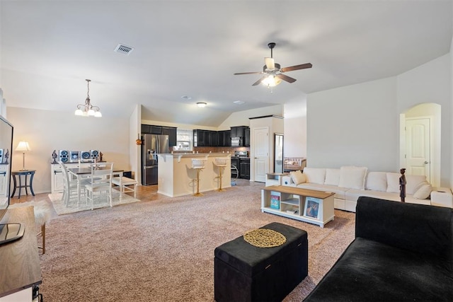 carpeted living room featuring ceiling fan with notable chandelier and vaulted ceiling