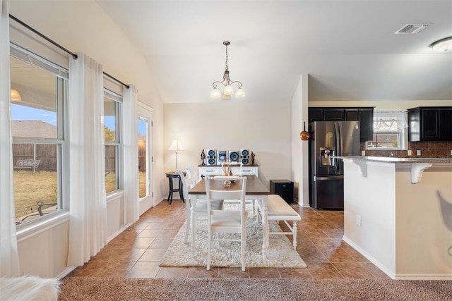 tiled dining space featuring a wealth of natural light, lofted ceiling, and an inviting chandelier