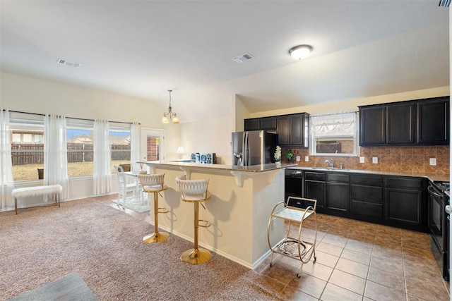 kitchen featuring decorative backsplash, black appliances, pendant lighting, a center island, and a breakfast bar area