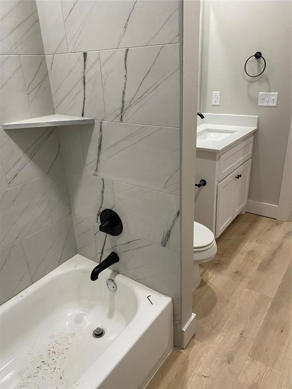 full bathroom with tiled shower / bath combo, vanity, hardwood / wood-style floors, and toilet