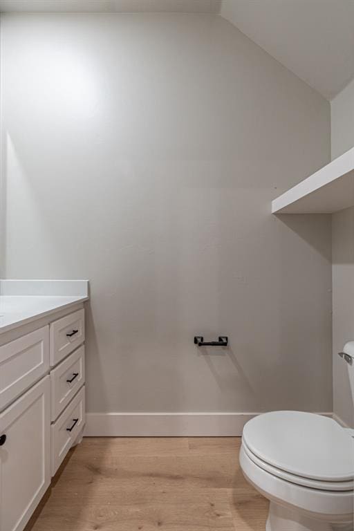 bathroom featuring hardwood / wood-style flooring, vanity, toilet, and lofted ceiling