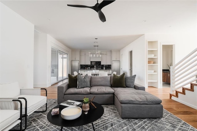 living room with hardwood / wood-style flooring, built in shelves, and ceiling fan with notable chandelier