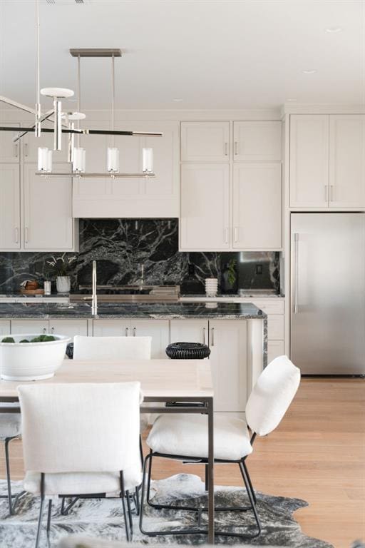 kitchen featuring built in fridge, hanging light fixtures, and white cabinets