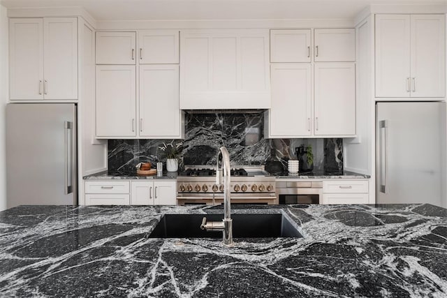 kitchen featuring white cabinets, decorative backsplash, dark stone counters, and high quality appliances