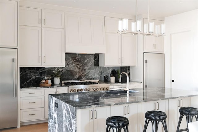 kitchen featuring dark stone countertops, built in refrigerator, and white cabinets