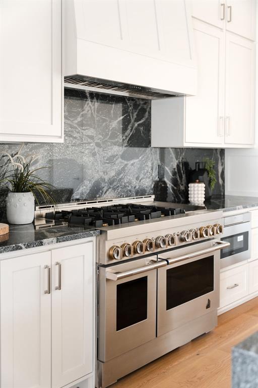 kitchen featuring white cabinetry, double oven range, dark stone counters, and premium range hood