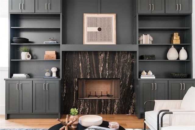 living room with built in features, a high end fireplace, and light hardwood / wood-style flooring