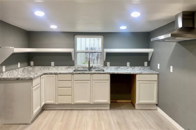 kitchen with light stone countertops, sink, wall chimney exhaust hood, white cabinets, and light wood-type flooring