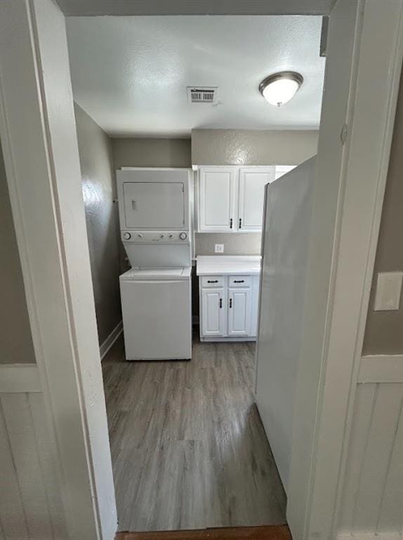 laundry area featuring cabinets, light wood-type flooring, and stacked washer / drying machine