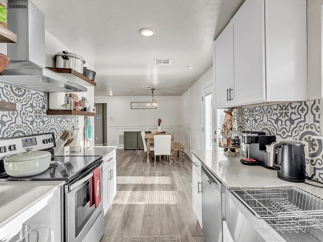 kitchen featuring appliances with stainless steel finishes, backsplash, light wood-type flooring, extractor fan, and white cabinetry