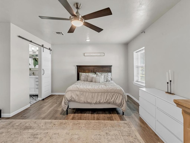 bedroom with a barn door, ceiling fan, sink, and wood-type flooring