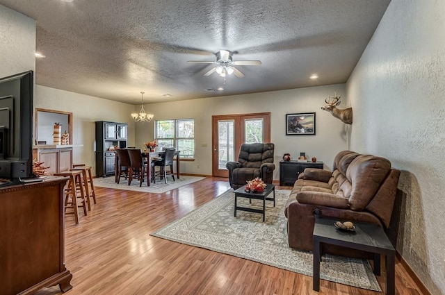 living room with ceiling fan with notable chandelier, a textured ceiling, and light wood-type flooring