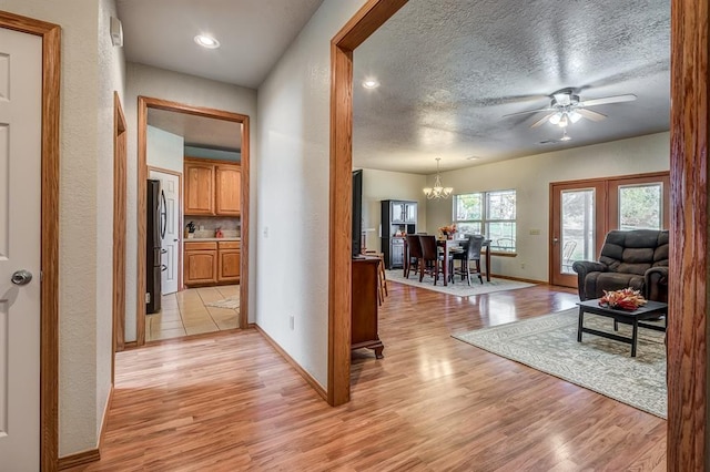 hall with light hardwood / wood-style floors, a textured ceiling, and a notable chandelier