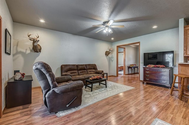 living room featuring ceiling fan, light wood-type flooring, and a textured ceiling