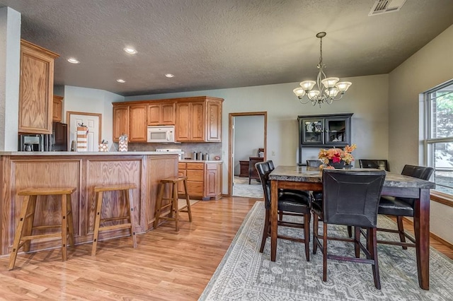 dining space with a textured ceiling, light hardwood / wood-style flooring, and an inviting chandelier