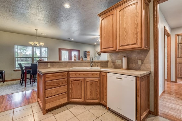 kitchen with a textured ceiling, white dishwasher, sink, decorative light fixtures, and light hardwood / wood-style flooring