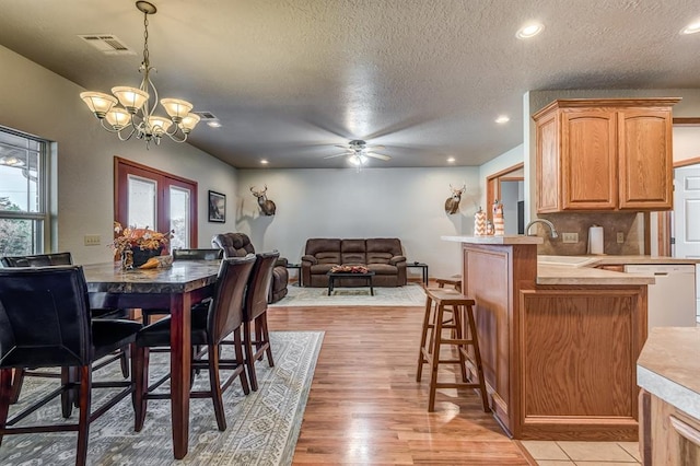 dining space featuring a textured ceiling, ceiling fan with notable chandelier, sink, and light hardwood / wood-style flooring