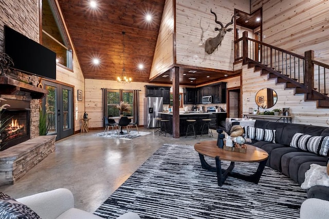 living room featuring a towering ceiling, a stone fireplace, concrete floors, a chandelier, and wood walls