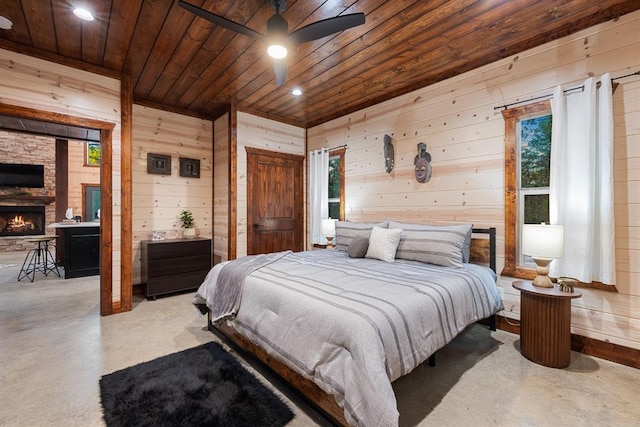 bedroom with multiple windows, a stone fireplace, wooden walls, and wood ceiling