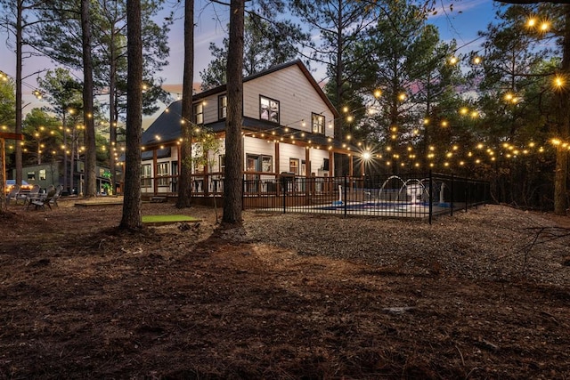 back house at dusk with a balcony and a fenced in pool