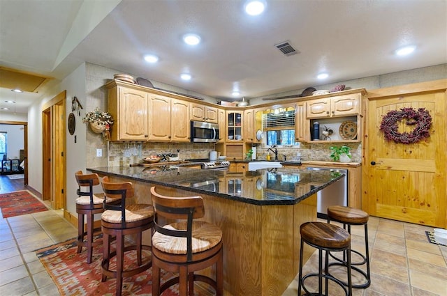 kitchen with stainless steel appliances, tasteful backsplash, kitchen peninsula, dark stone counters, and a kitchen bar