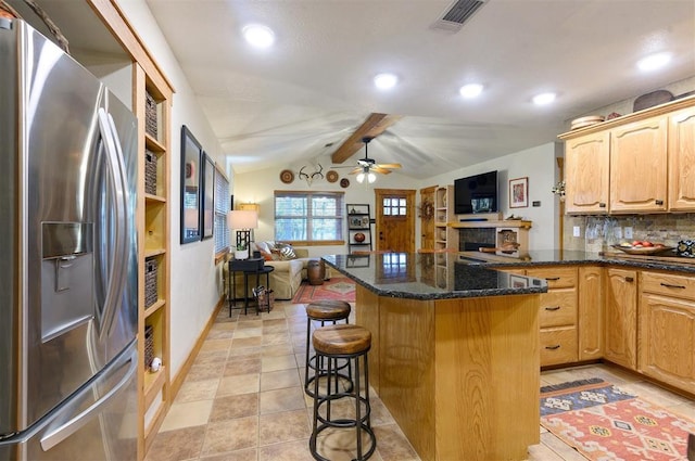 kitchen with dark stone counters, lofted ceiling with beams, ceiling fan, stainless steel fridge, and tasteful backsplash