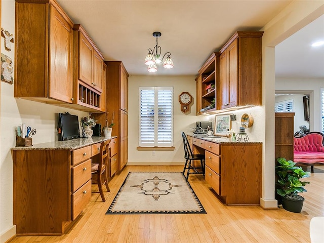 kitchen with light hardwood / wood-style floors, hanging light fixtures, light stone countertops, a chandelier, and built in desk