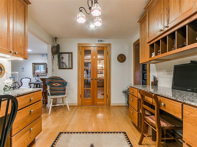 kitchen with hanging light fixtures, light wood-type flooring, french doors, and light stone counters