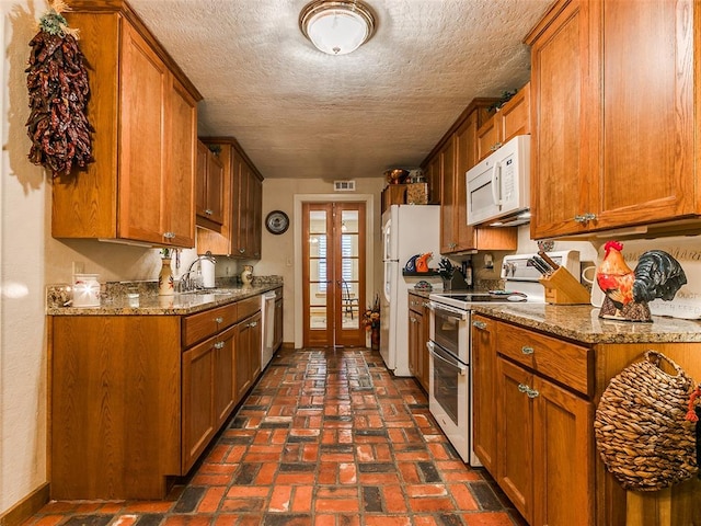 kitchen with sink, white appliances, a textured ceiling, french doors, and stone countertops