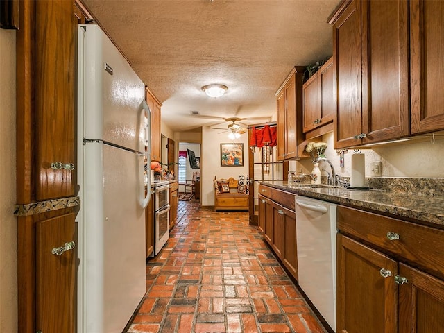 kitchen with ceiling fan, white appliances, dark stone countertops, a textured ceiling, and sink