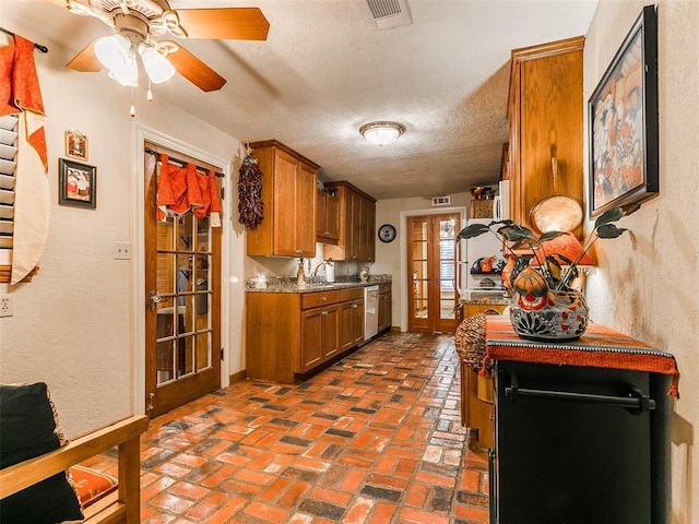 kitchen featuring dishwasher, stone counters, sink, a textured ceiling, and french doors