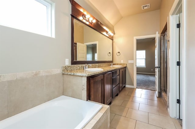 bathroom with tile patterned flooring, vanity, lofted ceiling, and tiled tub