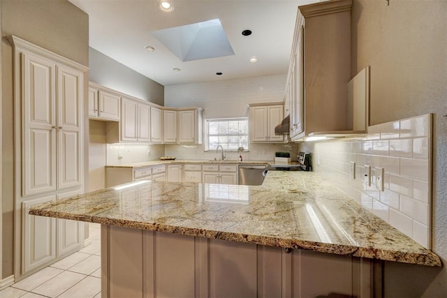 kitchen featuring a skylight, light stone countertops, sink, kitchen peninsula, and appliances with stainless steel finishes