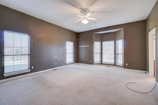 spare room with light colored carpet, a wealth of natural light, and ceiling fan