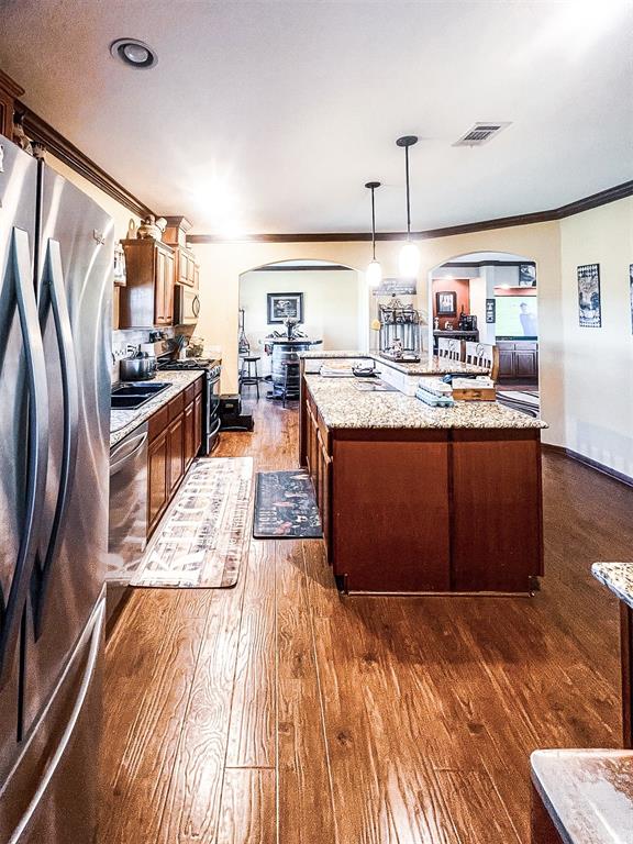 kitchen with pendant lighting, a center island, dark wood-type flooring, light stone countertops, and appliances with stainless steel finishes