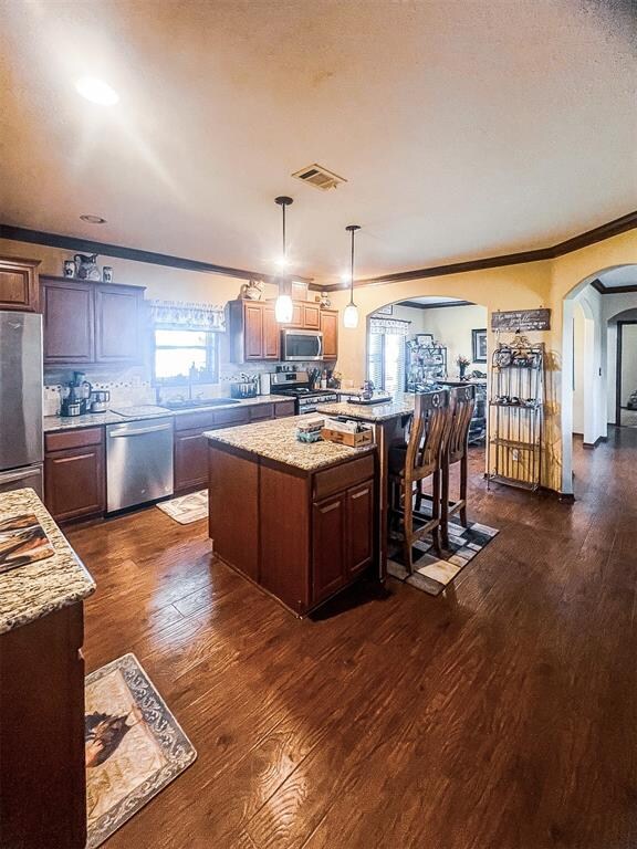 kitchen with a center island, dark wood-type flooring, hanging light fixtures, crown molding, and appliances with stainless steel finishes