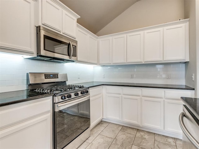 2213 Waterbrook Ct, Norman, OK 73026 - kitchen featuring appliances with stainless steel finishes, vaulted ceiling, dark countertops, white cabinetry, and light marble finish flooring