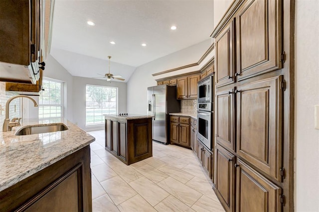 kitchen featuring light stone countertops, stainless steel appliances, vaulted ceiling, sink, and a center island