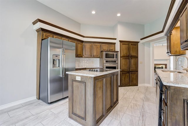 kitchen with decorative backsplash, appliances with stainless steel finishes, light stone countertops, sink, and a kitchen island