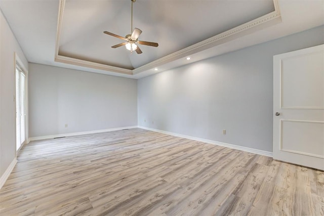 empty room with light wood-type flooring, a tray ceiling, and ceiling fan