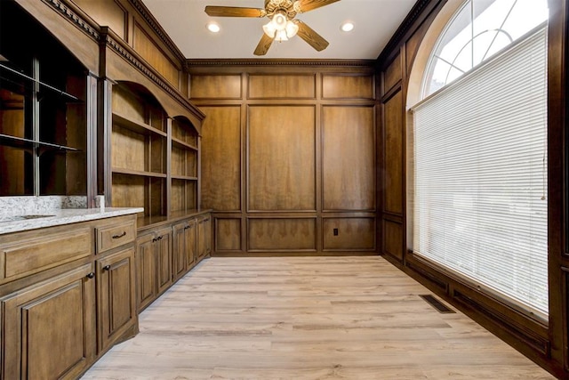 unfurnished office with wooden walls, light hardwood / wood-style floors, ceiling fan, and ornamental molding