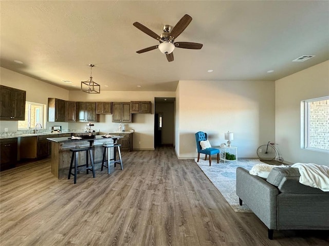 kitchen with ceiling fan, light hardwood / wood-style flooring, pendant lighting, a breakfast bar, and a kitchen island