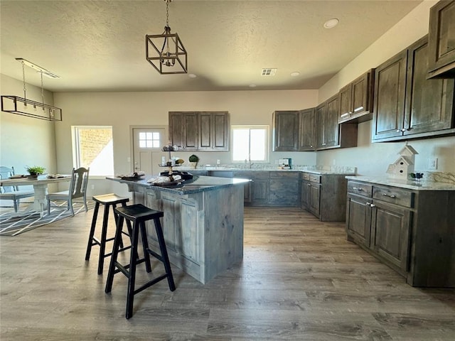 kitchen featuring a kitchen bar, a textured ceiling, pendant lighting, wood-type flooring, and a kitchen island