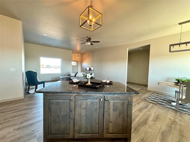 kitchen with dark stone counters, dark brown cabinetry, hardwood / wood-style flooring, a center island, and hanging light fixtures