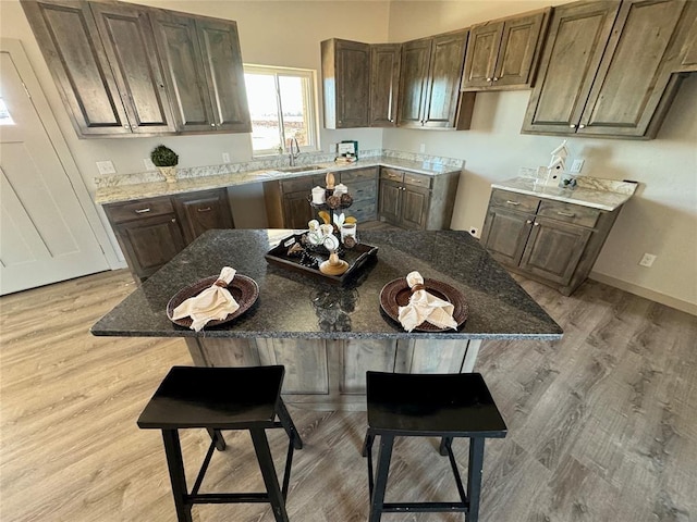 kitchen with dark brown cabinetry, stone counters, sink, a kitchen island, and light wood-type flooring